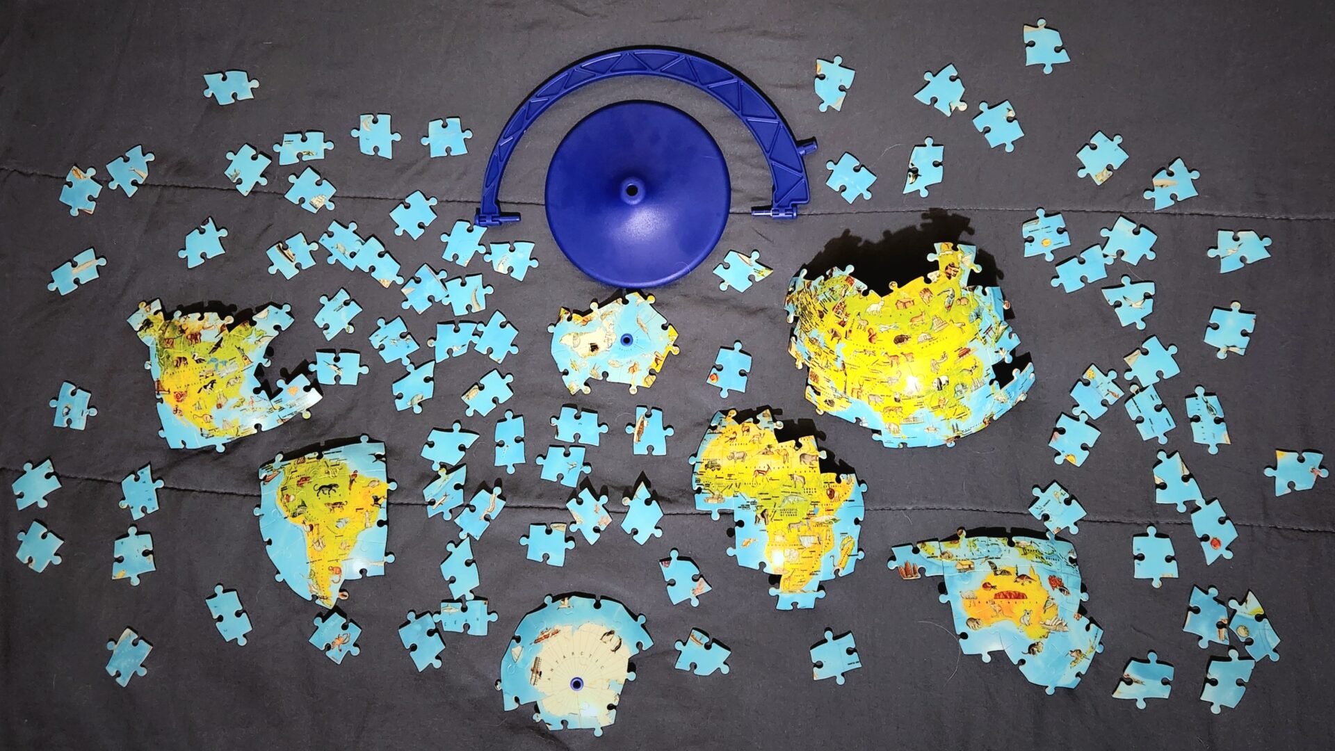 Partially assembled collection of major continents from a puzzle globe separately lying flat on a bed.